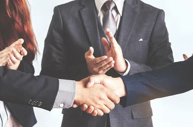 business people shaking hands while others clap