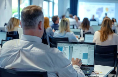 A high-angle view of a compliance training session, with employees taking notes and engaging with interactive compliance software on their laptops.