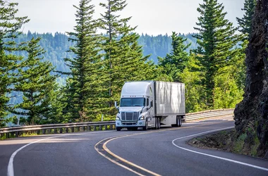 truck driving up a road by a forest