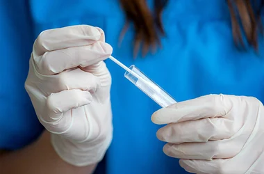 Medical Technician putting a swab of oral fluid into a test tube