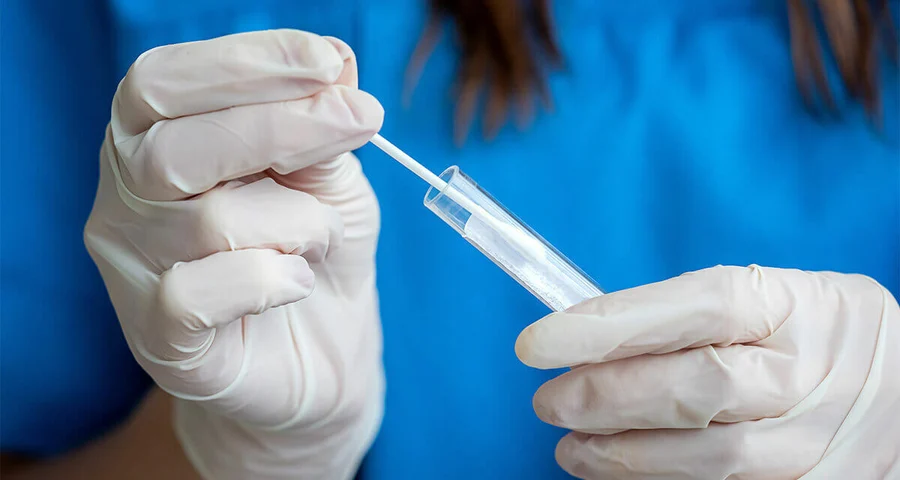 Medical Technician putting a swab of oral fluid into a test tube