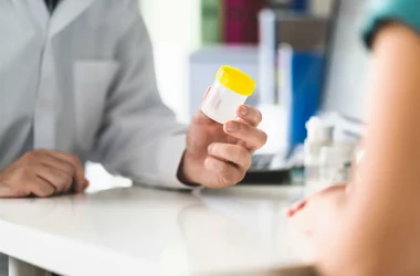 medical technician handing an empty urine specimen cup to a patient