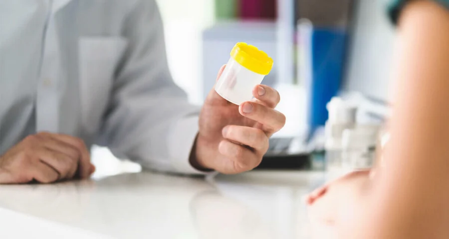 medical technician handing an empty urine specimen cup to a patient