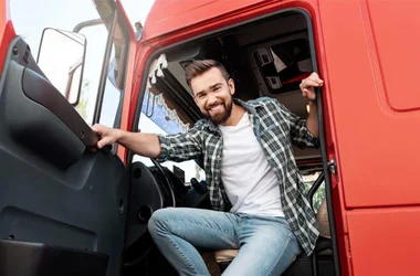Young smiling male truck driver inside his red cargo truck