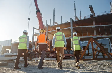 Diverse Team of Specialists Inspect Commercial, Industrial Building Construction Site. Real Estate Project with Civil Engineer, Investor and Worker. In the Background Crane, Skyscraper Formwork Frames