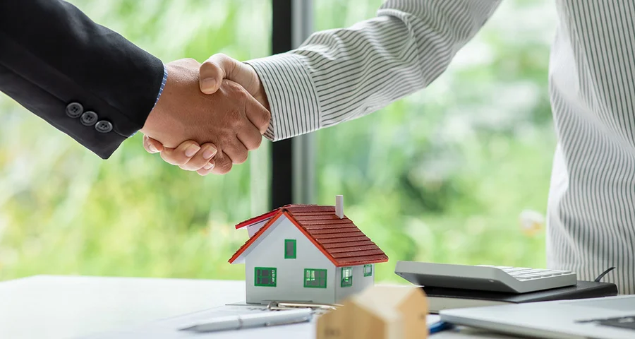 Realtor and client shake hands over mini house