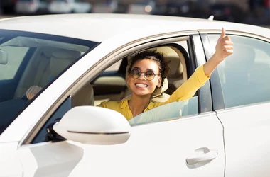 cheerful woman with sunglasses driving with thumbs-up