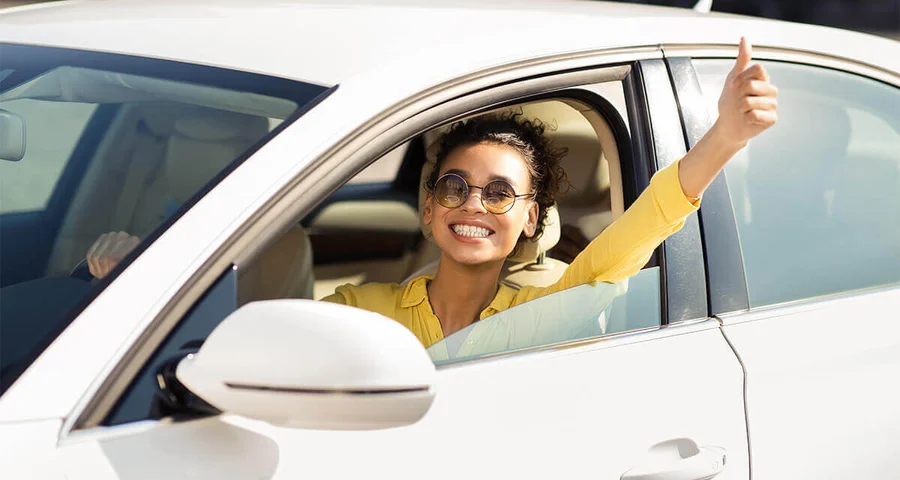 cheerful woman with sunglasses driving with thumbs-up