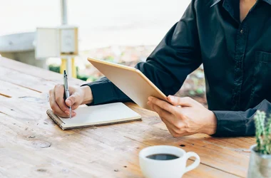person taking notes on paper while holding tablet