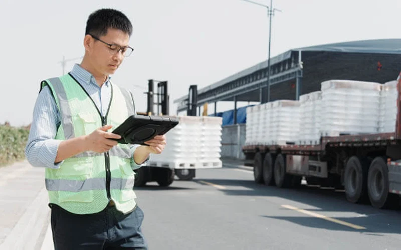 Logistics worker in safety vest using tablet to inspect cargo on truck at distribution center