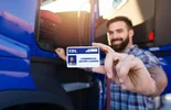 Portrait of middle aged bearded truck driver standing by his truck and showing his commercial driver license