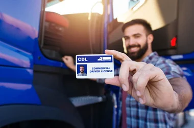 Portrait of middle aged bearded truck driver standing by his truck and showing his commercial driver license