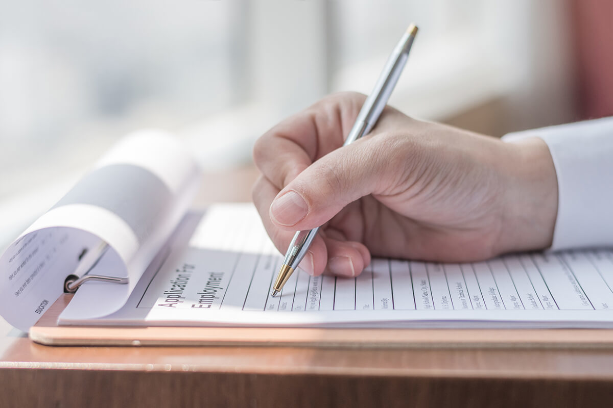 Hand holding a pen filling out an application for employment