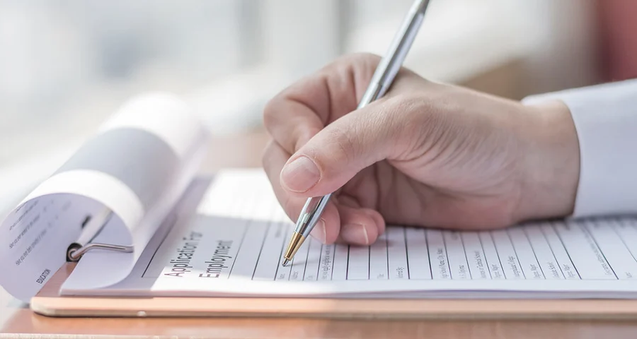 Hand holding a pen filling out an application for employment