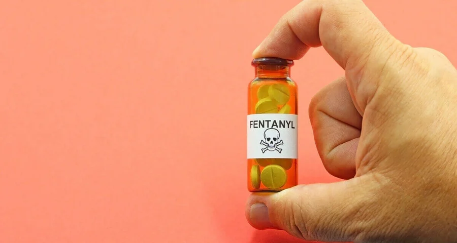 Hand holding a brown vial filled with pills labeled Fentanyl with a skull and crossbones