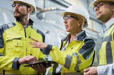 Industrial worker wearing hard hats and safety vests having an onsite meeting