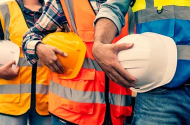 Industrial workers lined up holding their safety helmets at their waistline