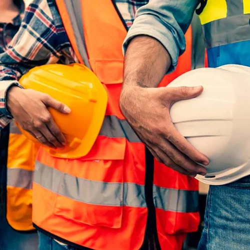 Industrial workers lined up holding their safety helmets at their waistline