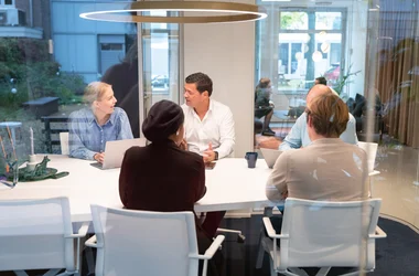 Grupp av kollegor sitter runt ett bord och diskuterar