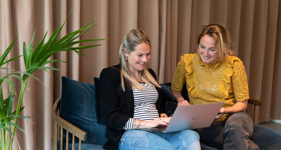 Two women sitting in a sofa looking at a computer