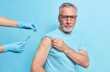 man pointing to a blue bandaid on his shoulder where he was given an immunization shot.