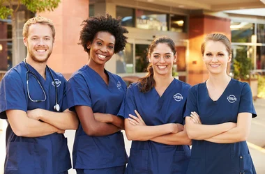4 nurses wearing DISA scrubs standing together with arms crossed