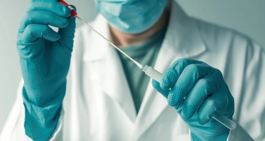 medical technician putting a swab with oral fluid into a test tube