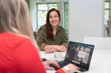 Smiling female candidate sitting with arms on table talking to interviewer