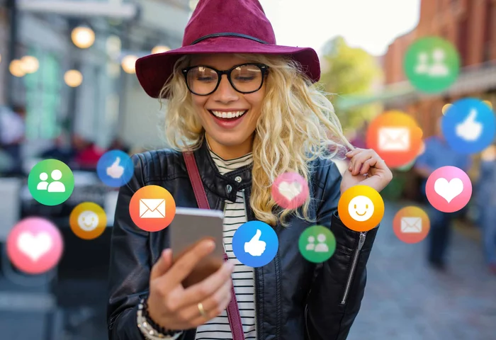 En glad kvinna tittar på sin telefon där olika sociala mediekonton syns